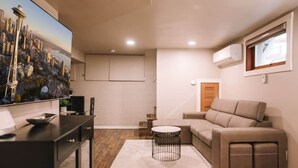 Un salon moderne avec un canapé d’angle, une petite table ronde, un meuble TV noir et un tableau représentant un paysage urbain accroché au mur.