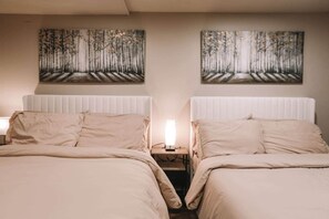 A hotel room with two beds, a nightstand, a lamp, and two forest-themed wall art pieces.