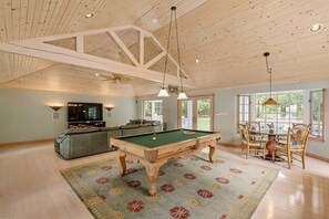 Een ruime kamer met een pooltafel, een bank, een eettafel met stoelen en een televisie.