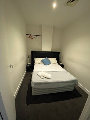 A neatly made bed with a white comforter and a blue pillow, a black headboard, and a small bedside table with a lamp. - Collins central 2-bd apartment. Tramstop 5 CBD access (Melbourne)