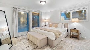 A bedroom with a large bed, a nightstand, a mirror, and a window with curtains.