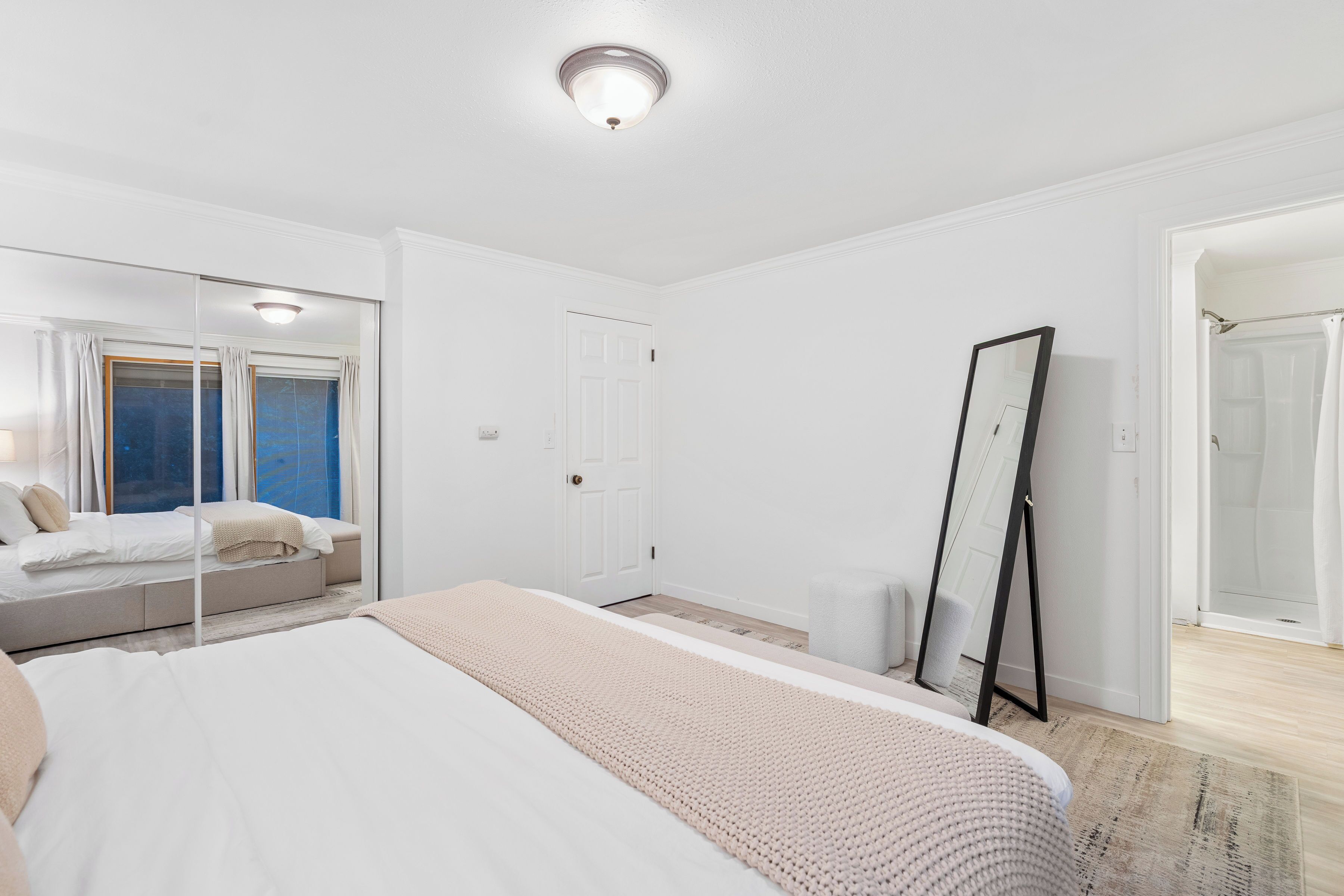 Un dormitorio con una cama grande, un espejo de tocador, un armario y una ventana con cortinas.