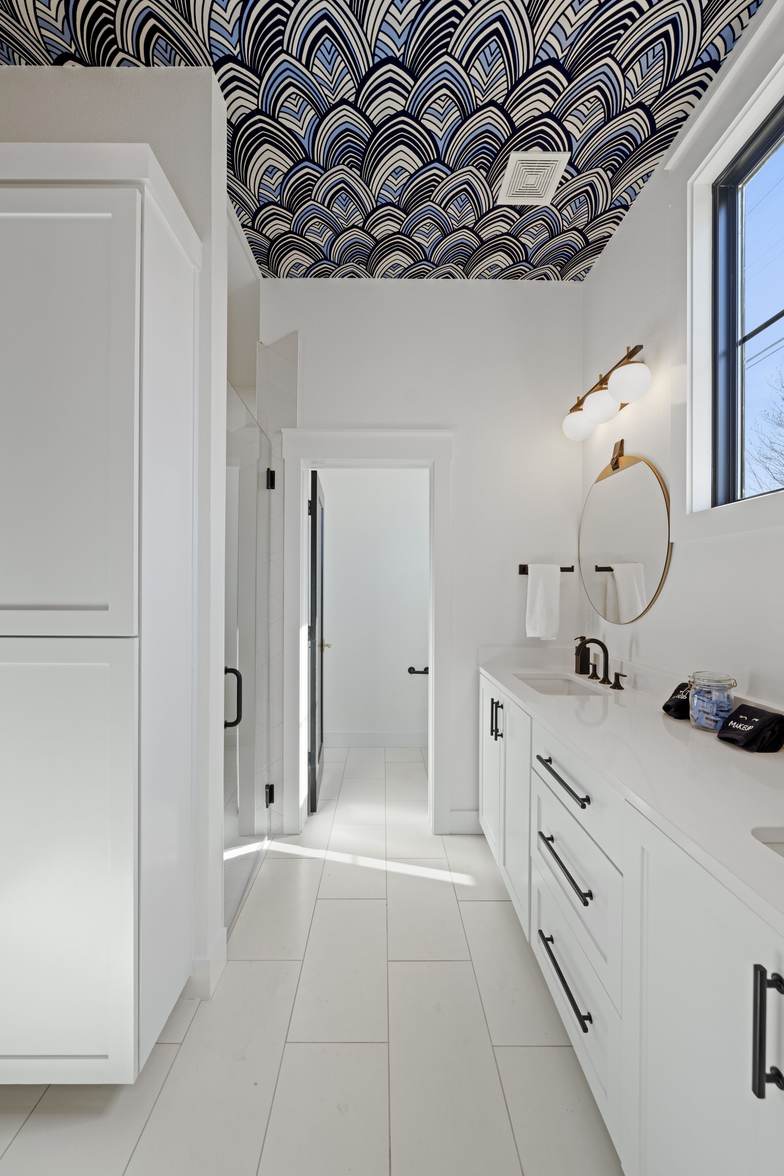 Un baño moderno con muebles blancos, un espejo grande y un techo estampado.