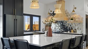 A modern kitchen with a large island, black chairs, and pendant lighting.