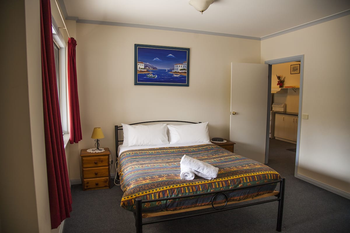 A neatly made bed with a patterned bedspread, a bedside table with a lamp, and a painting on the wall.