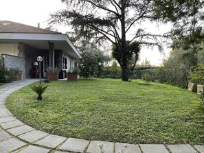 A residential property with a well-maintained lawn, a large tree, and a house with a tiled roof and a porch.