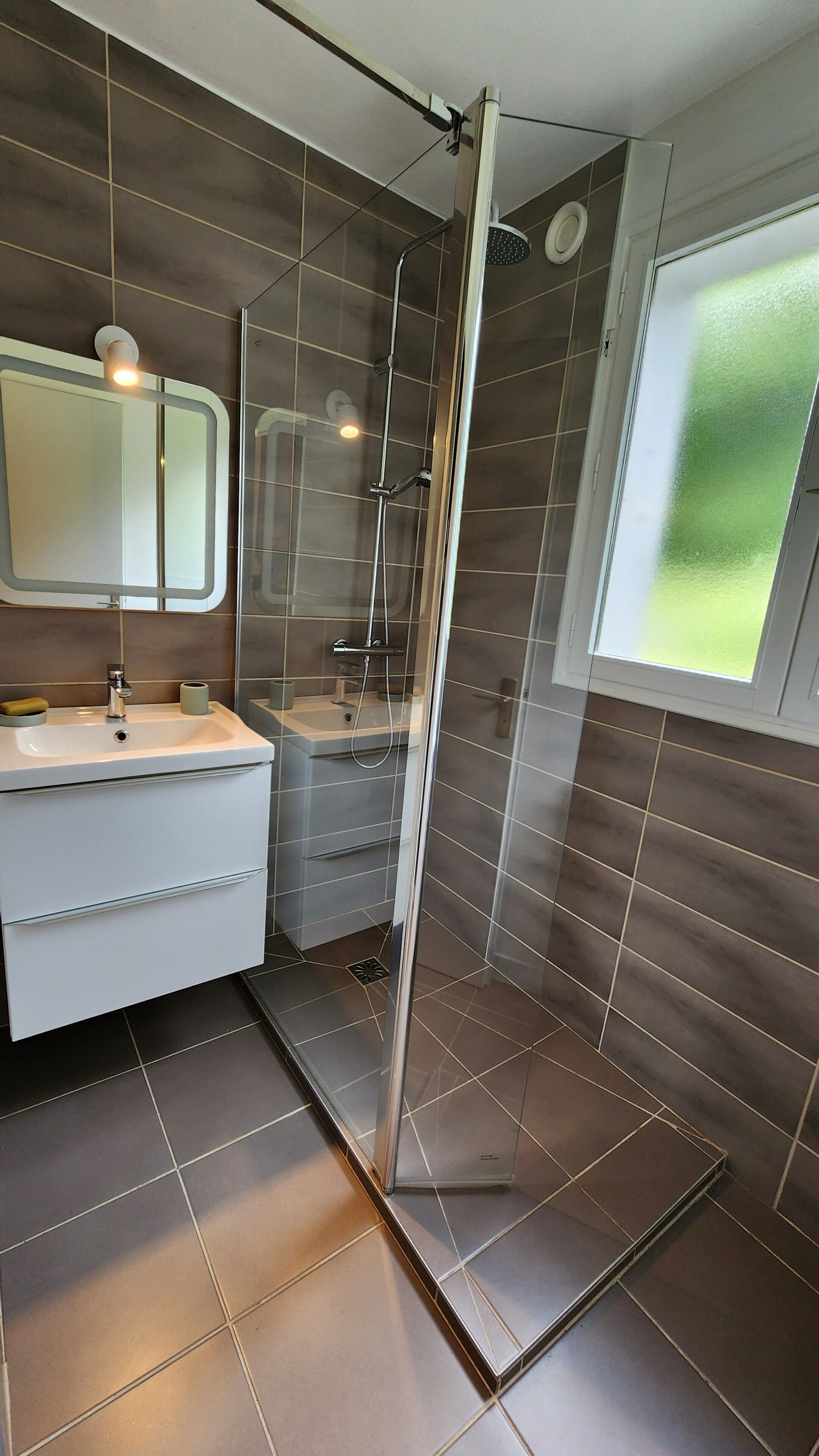 A modern bathroom with a glass-enclosed shower, a sink with a mirror, and a window providing a view.