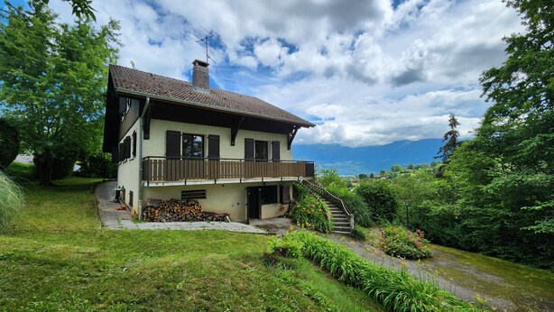 Ein zweistöckiges Haus mit Balkon, umgeben von üppiger Vegetation und einem malerischen Bergblick.
