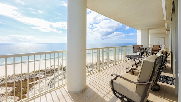 A balcony with a view of the beach and ocean. There are chairs and a table.