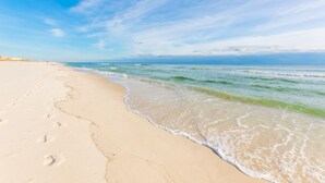 A beach with footprints leading to the water, a clear sky, and gentle waves.