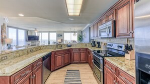 A spacious kitchen with granite countertops, wooden cabinets, stainless steel appliances, and a large window providing natural light.