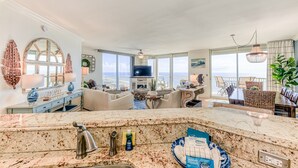 A spacious living area with a large TV, a dining table, and a balcony with a view.