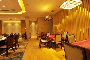A hotel dining area with multiple tables and chairs, a patterned carpet, and a decorative wall.