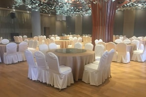 Une salle de banquet avec des tables rondes et des chaises blanches, disposées en rangées.