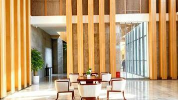 A spacious lobby with a marble floor, a wooden reception desk, and a seating area with chairs and a table.