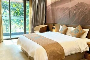 Et hotelværelse med seng, sofa, stort vindue og udsigt til et bjerg.