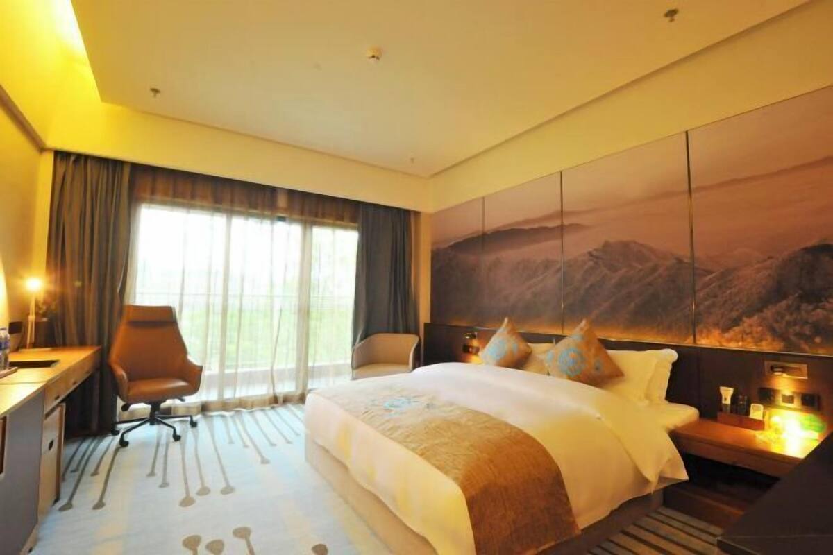 Habitación de hotel con una cama grande, un escritorio, una silla y vistas a las montañas desde la ventana.