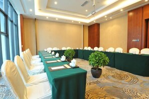 Een congreszaal met een lange tafel, stoelen en kamerplanten.