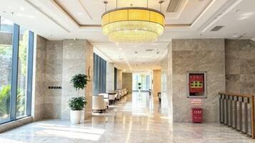 A hotel lobby with a marble floor, a chandelier, a reception desk, and a plant.