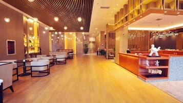 A hotel lobby with a wooden floor, seating area, reception desk, and a staircase.
