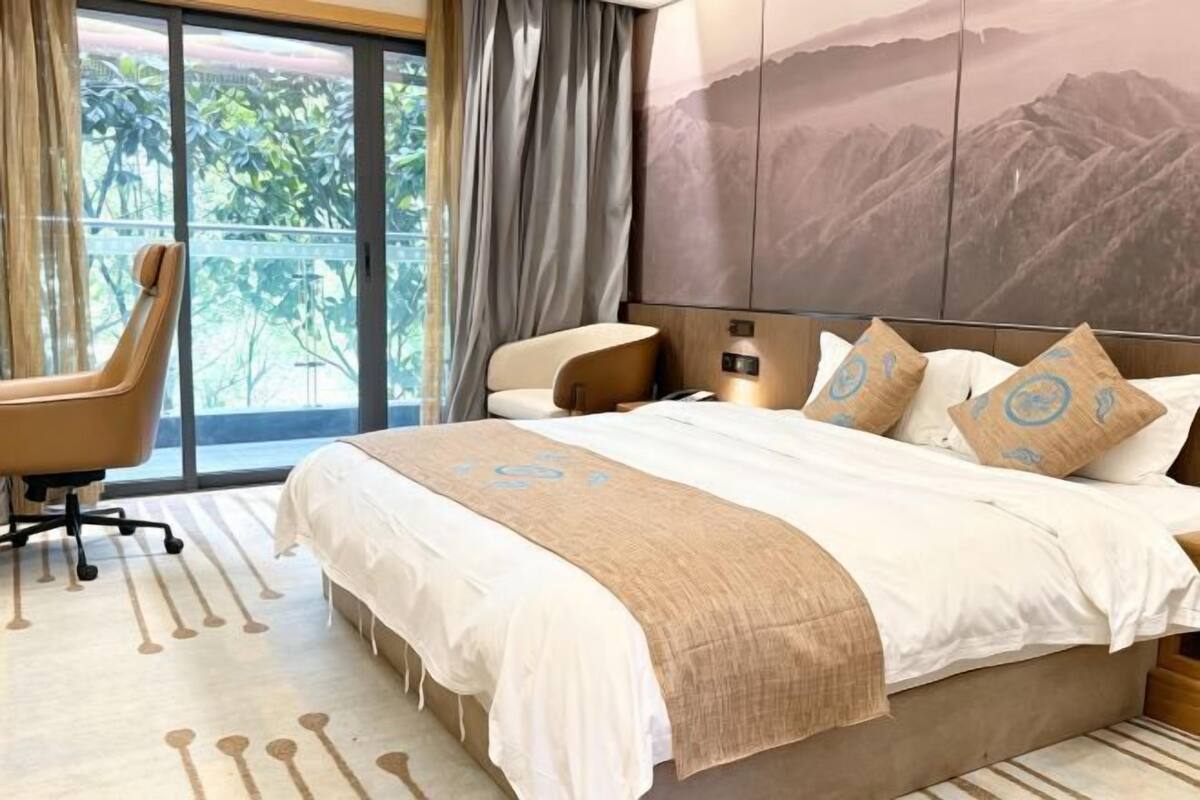 Habitación de hotel con una cama grande, un escritorio y vista a zonas verdes por la ventana.