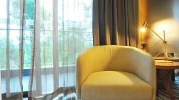 A room with a yellow armchair, a desk with a lamp, and sheer curtains allowing natural light.