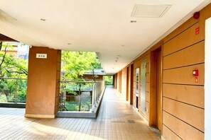 A corridor with a glass railing, a tiled floor, and a wooden wall with a fire alarm.