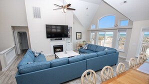A spacious living room with a large sectional sofa, a flat-screen TV, and a dining area with wooden chairs and a table. - OCEANFRONT, Private Pool, Pool Table, Ocean Views, BU70, Kings Landing (Corolla)