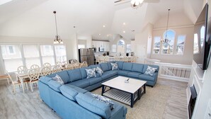 A spacious living area with a large blue sectional sofa, a coffee table, and a dining set. - OCEANFRONT, Private Pool, Pool Table, Ocean Views, BU70, Kings Landing (Corolla)