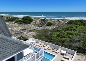 Une piscine sur le toit avec vue sur l’océan, une terrasse en bois et un escalier menant à la plage.