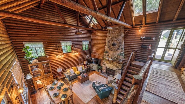 A spacious log cabin interior with a dining area, seating, a fireplace, and a staircase.