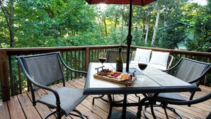 A wooden deck with a table and chairs, a bottle of wine, and a glass of wine.