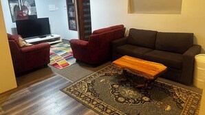 A living room with a brown sofa, two red armchairs, a wooden coffee table, a TV, and a patterned rug. - Quaint Flat, near hospitals, Very central, internet (Geraldton)