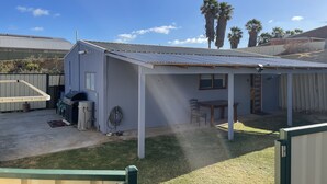A small, single-story building with a metal roof, a patio area with a table and chairs, and a covered outdoor space. - Quaint Flat, near hospitals, Very central, internet (Geraldton)