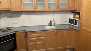 A kitchen with wooden cabinets, a microwave, a sink, and a stove. - Quaint Flat, near hospitals, Very central, internet (Geraldton)