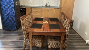 A dining area with a wooden table and four chairs, a kitchen with wooden cabinets, and a blue refrigerator. - Quaint Flat, near hospitals, Very central, internet (Geraldton)