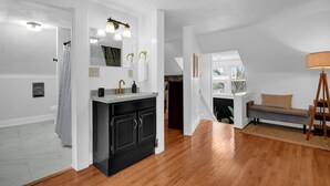 A modern interior with a kitchen area featuring a black cabinet and a white countertop, a wooden floor, and a seating area with a sofa and a lamp.