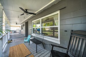 A covered porch with a ceiling fan, a table and two chairs, and a window with blinds.