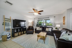 A living room with a TV, leather sofas, a coffee table, and a ceiling fan.