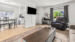 A modern living room with a flat-screen TV, a dark leather sofa, a wooden coffee table, and a dining area with a wooden table and chairs. - Bright & Spacious 2 Bedroom | Quiet | Safe | Clean (Mount Clemens)