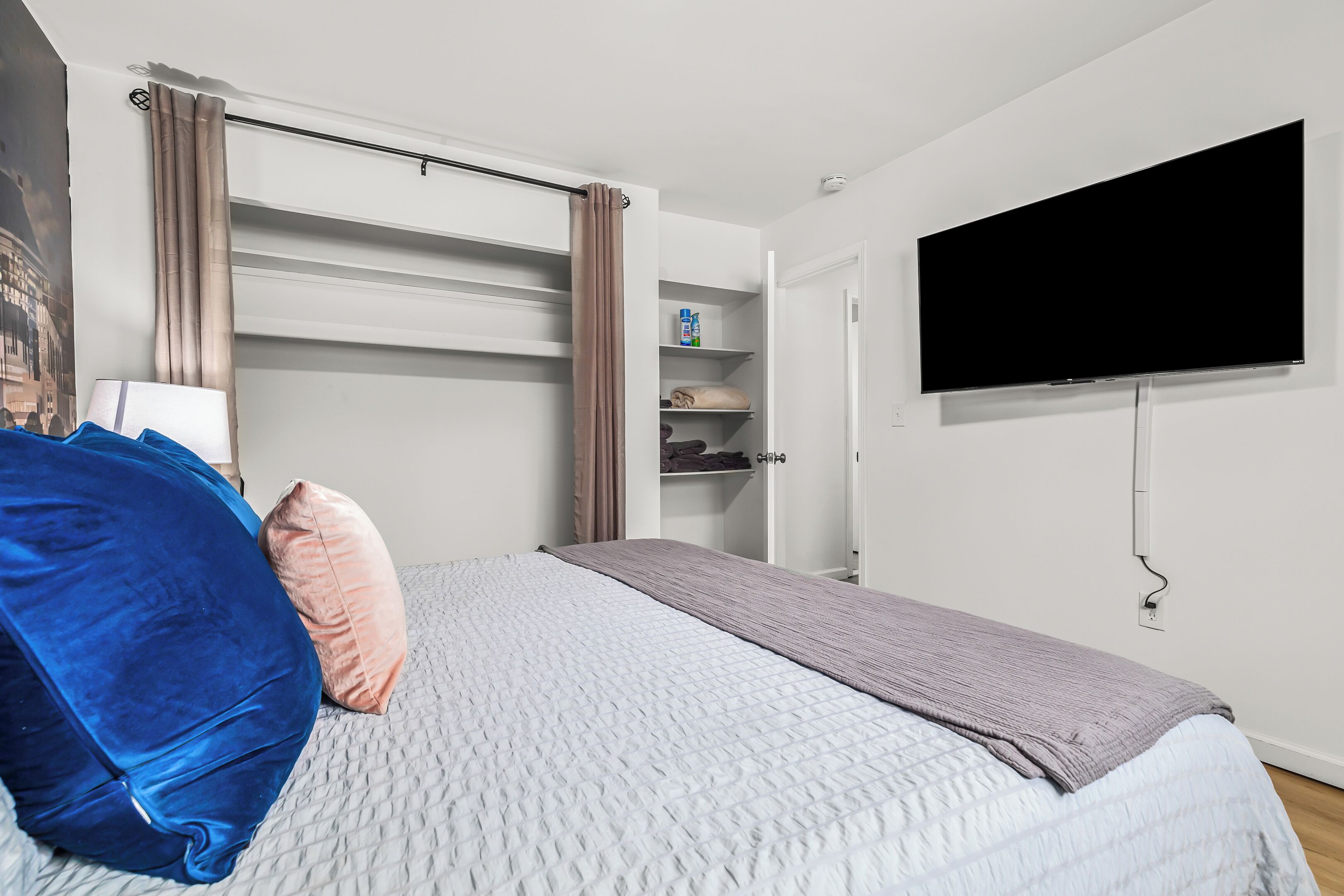 Ein Schlafzimmer mit einem Bett, einem an der Wand montierten Fernseher, einem Kleiderschrank und einem Regal mit Pflegeprodukten.