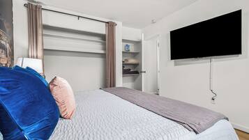 Ein Schlafzimmer mit einem Bett, einem an der Wand montierten Fernseher, einem Kleiderschrank und einem Regal mit Pflegeprodukten.