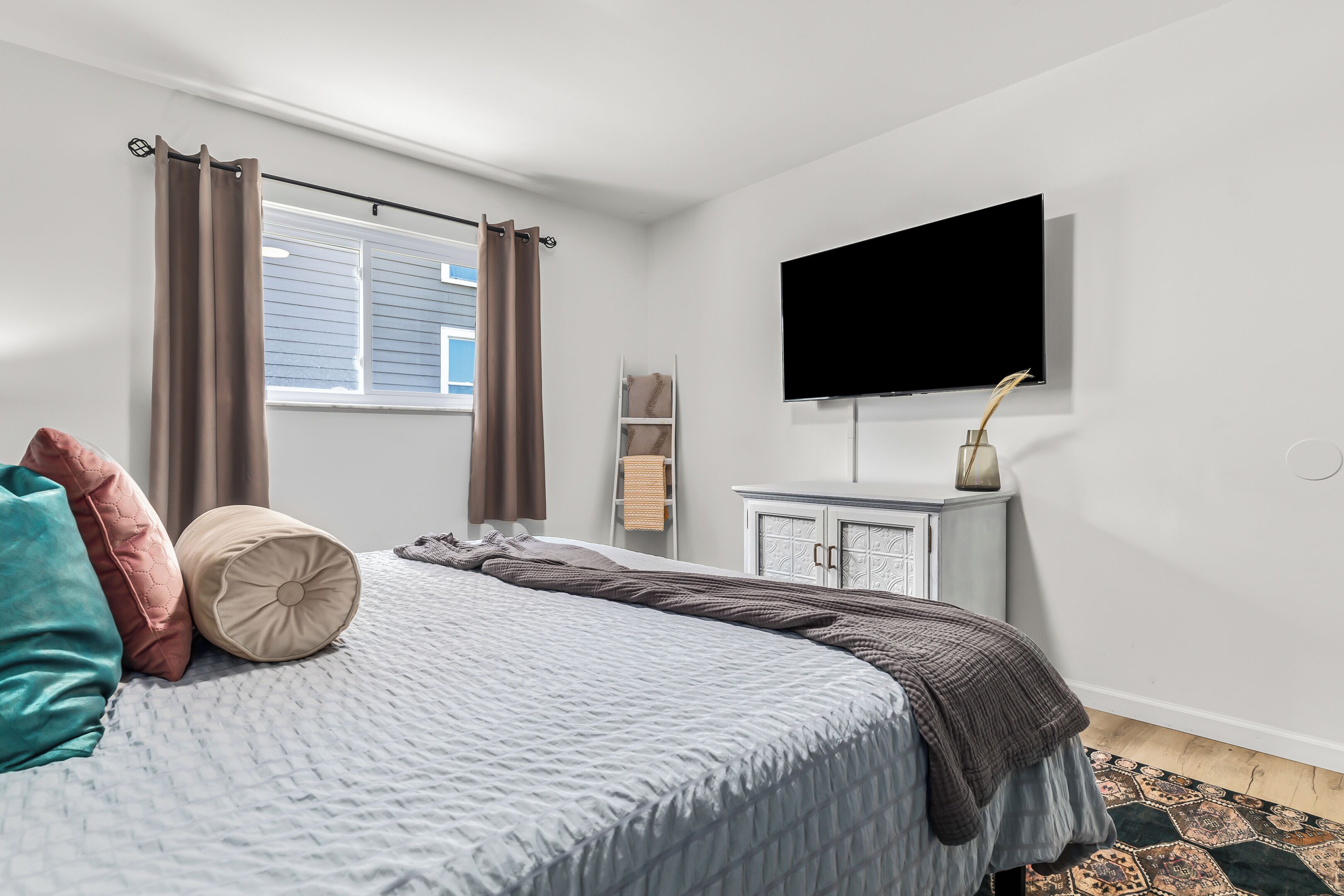A bedroom with a bed, a flat-screen TV, a dresser, and a window with curtains.