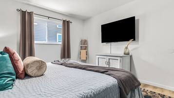 A bedroom with a bed, a flat-screen TV, a dresser, and a window with curtains.