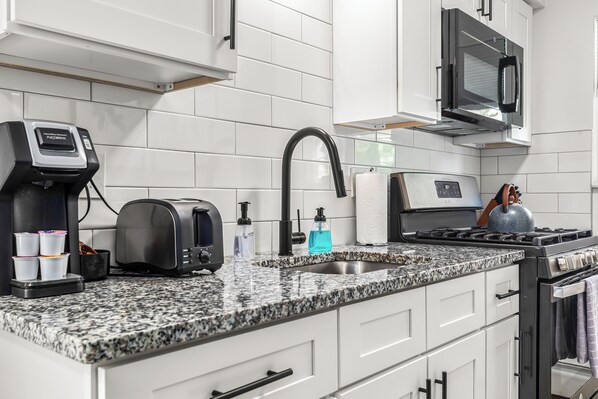 Eine moderne Küche mit weißen Schränken, einer Granitabdeckung, einer Kaffeemaschine, einem Toaster, einem Wasserkocher und einem Herd.