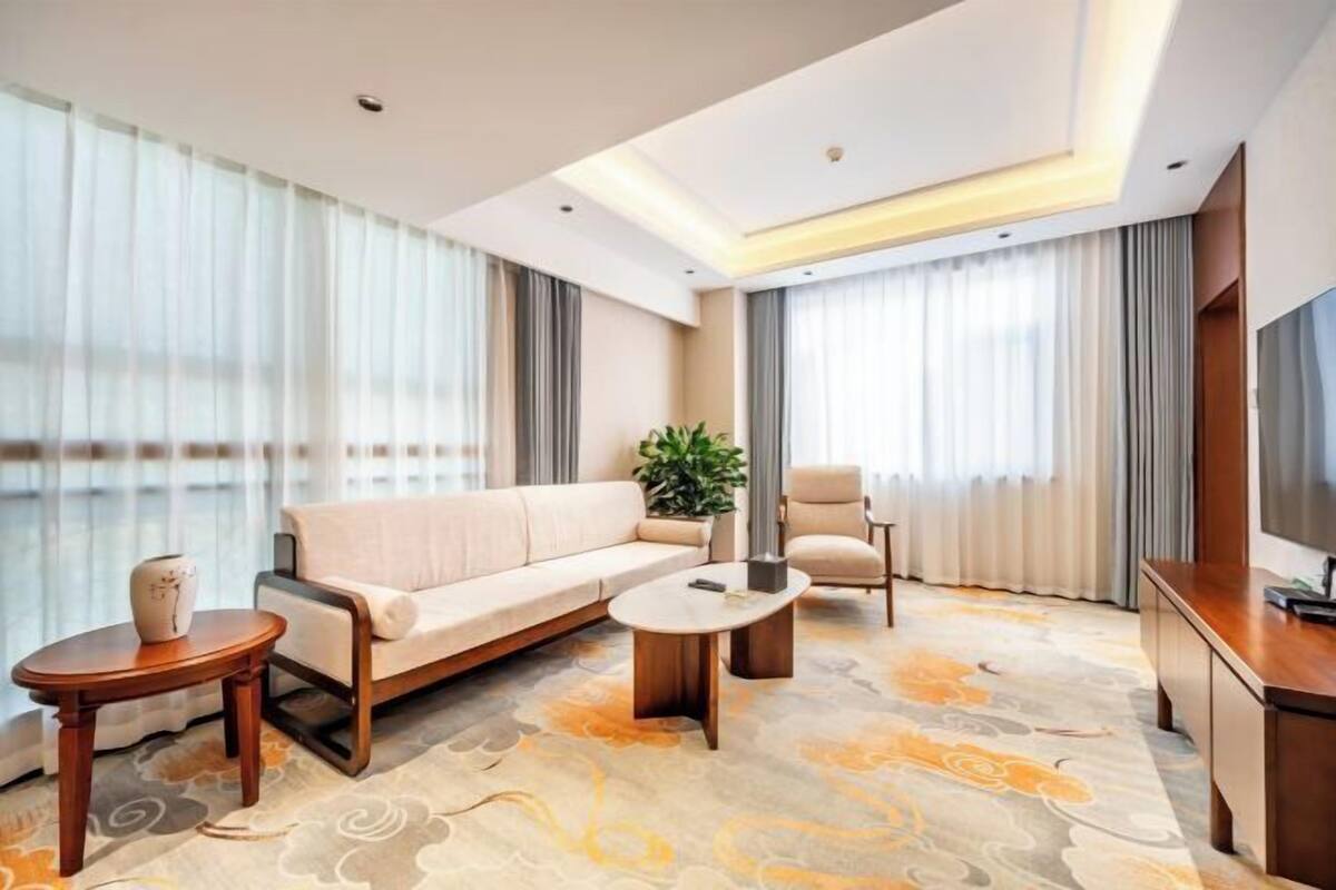 A modern hotel room with a sofa, armchair, coffee table, and a TV.