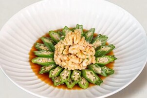 Un plato blanco con una porción de comida en el centro, rodeada de verduras verdes en un bol.