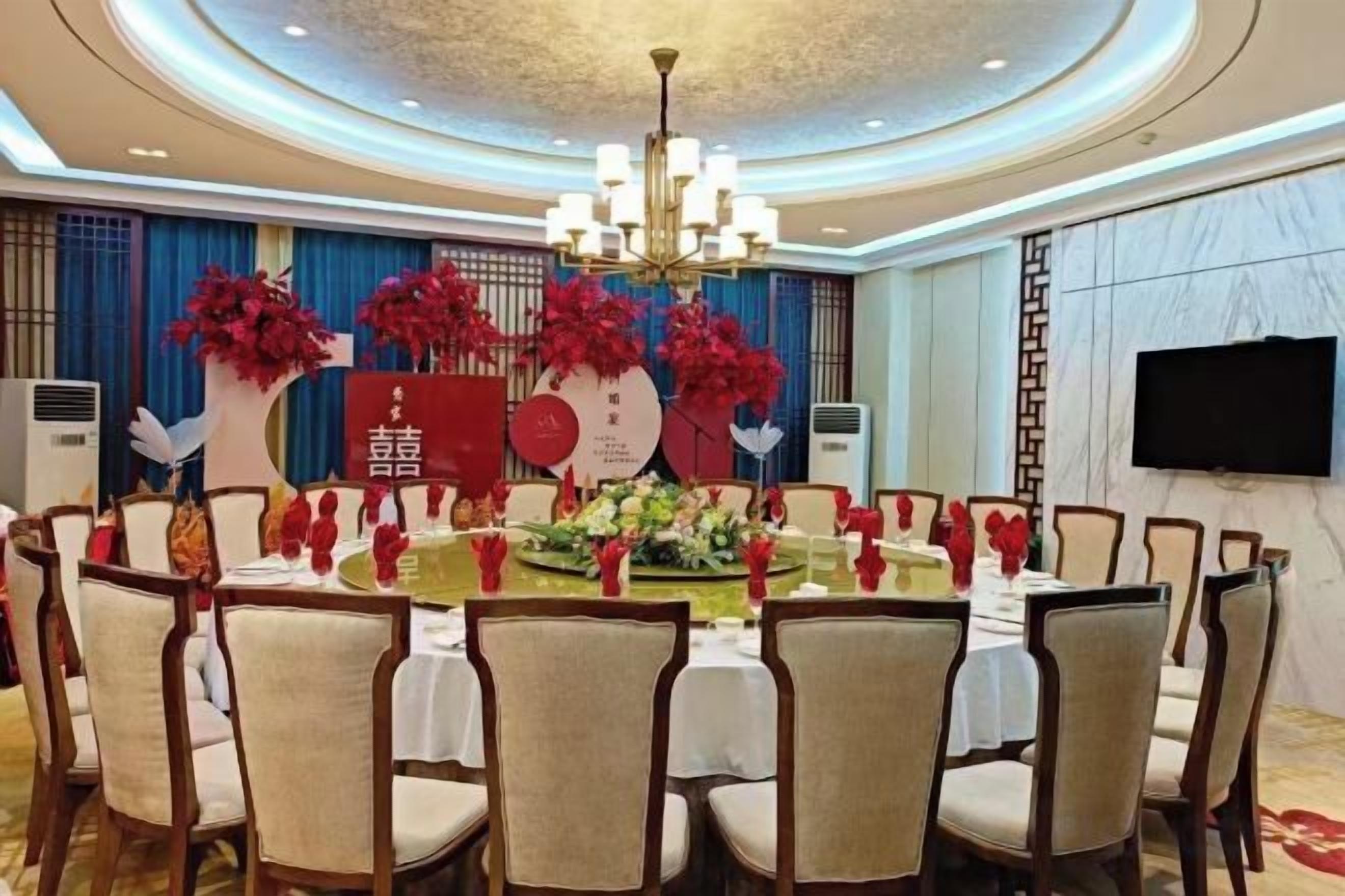 A conference room with a round table, chairs, a chandelier, and a decorative backdrop with floral arrangements.