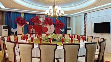 A conference room with a round table, chairs, a chandelier, and a decorative backdrop with floral arrangements.