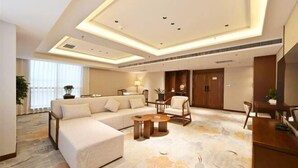 Una habitación de hotel moderna con un sofá modular, una mesita redonda y una zona de comedor con mesa y sillas.